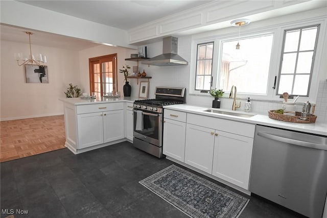 kitchen with wall chimney exhaust hood, sink, hanging light fixtures, appliances with stainless steel finishes, and kitchen peninsula