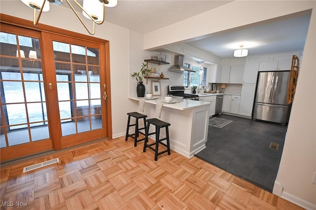 kitchen featuring wall chimney range hood, a breakfast bar area, appliances with stainless steel finishes, white cabinetry, and kitchen peninsula