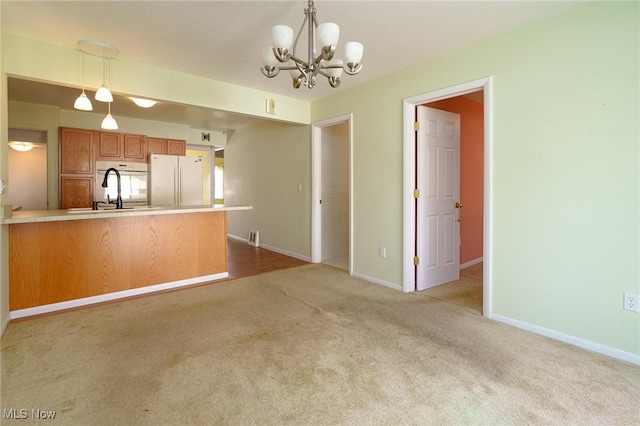 kitchen featuring white refrigerator, light colored carpet, decorative light fixtures, and sink