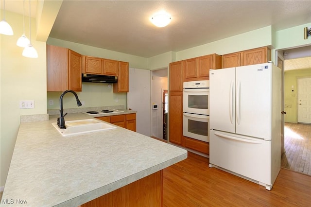 kitchen with decorative light fixtures, sink, white appliances, kitchen peninsula, and light wood-type flooring