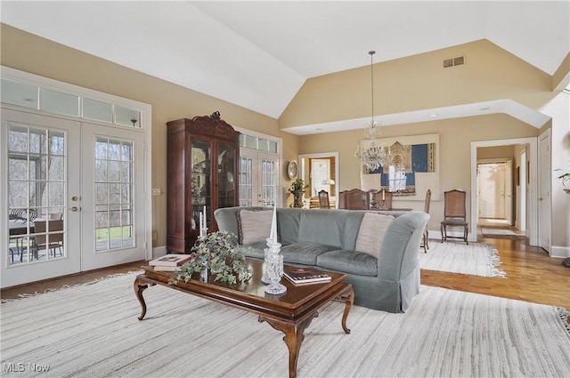 living room featuring vaulted ceiling, french doors, a chandelier, and light wood-type flooring