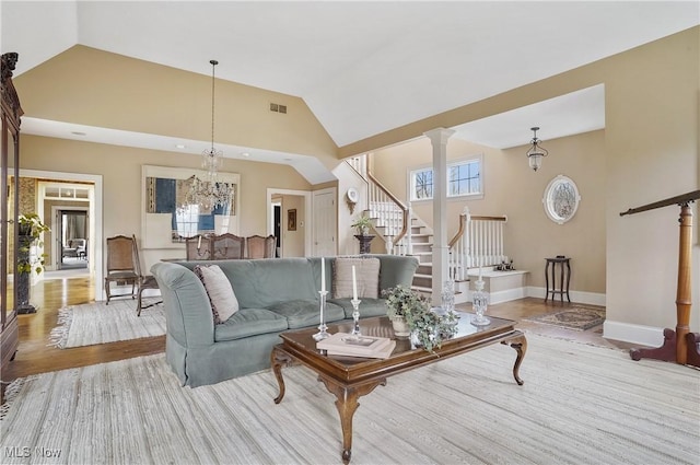 living room featuring a chandelier, light hardwood / wood-style floors, high vaulted ceiling, and ornate columns