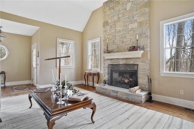 living room with a stone fireplace, light hardwood / wood-style flooring, and vaulted ceiling