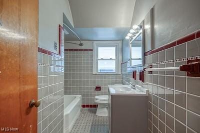 full bathroom featuring washtub / shower combination, vanity, toilet, and tile walls