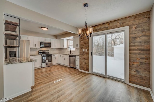 kitchen featuring pendant lighting, white cabinets, light hardwood / wood-style floors, light stone counters, and stainless steel appliances