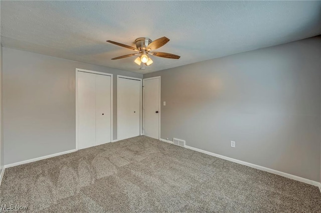 unfurnished bedroom with ceiling fan, a textured ceiling, carpet, and two closets