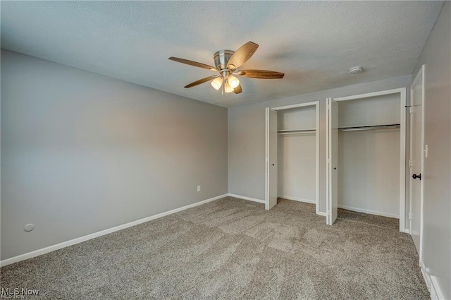 unfurnished bedroom with ceiling fan, two closets, light colored carpet, and a textured ceiling