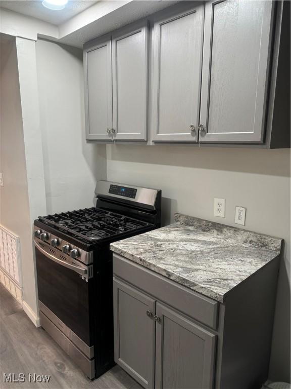 kitchen with gray cabinets, gas range, light stone countertops, and light hardwood / wood-style flooring