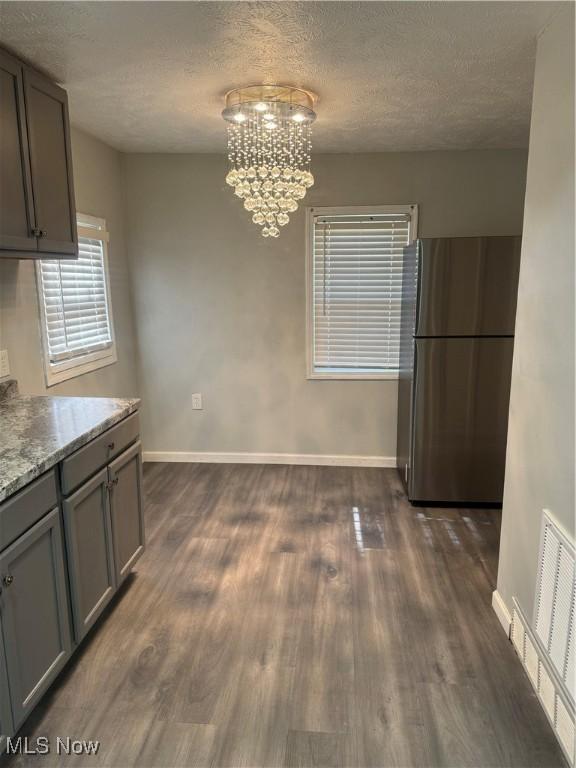 unfurnished dining area with a textured ceiling, a notable chandelier, and dark hardwood / wood-style flooring