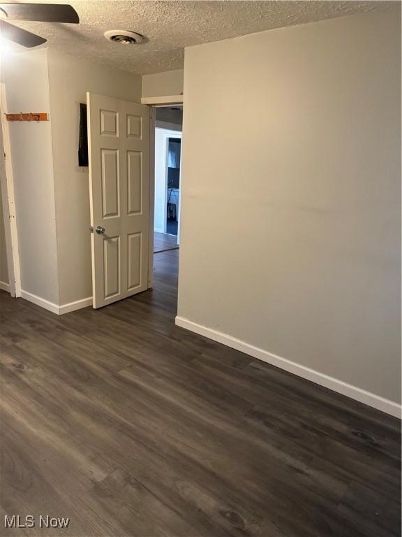 empty room with ceiling fan, dark hardwood / wood-style floors, and a textured ceiling