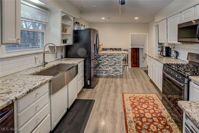 kitchen with light stone counters, appliances with stainless steel finishes, light wood-type flooring, and white cabinets