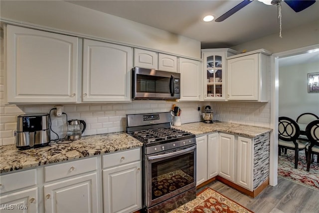 kitchen with stainless steel appliances, white cabinets, light stone counters, and decorative backsplash