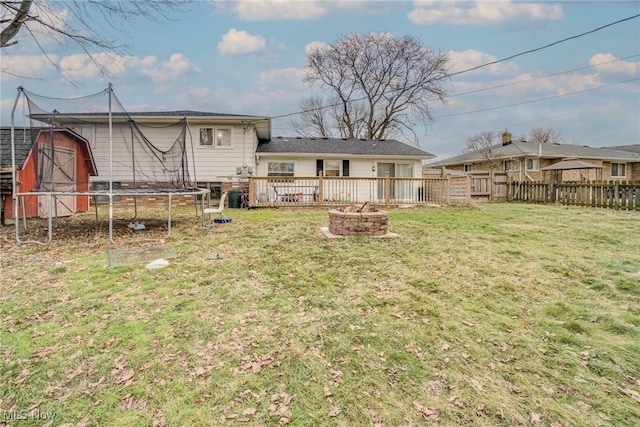 rear view of property featuring a trampoline, a fire pit, a lawn, and a deck