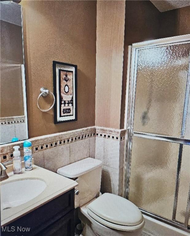 bathroom featuring vanity, a shower with door, toilet, and tile walls