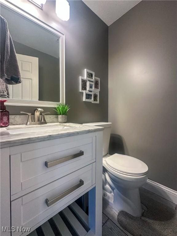 half bathroom with toilet, baseboards, and vanity