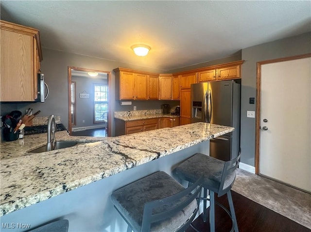 kitchen with light stone counters, a peninsula, a sink, a kitchen breakfast bar, and appliances with stainless steel finishes