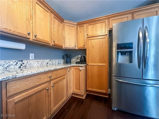 kitchen featuring stainless steel refrigerator with ice dispenser, dark hardwood / wood-style flooring, a textured ceiling, and light stone counters