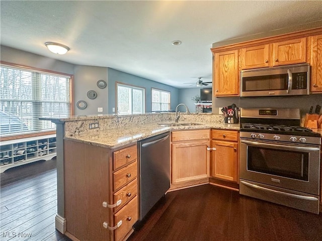 kitchen with light stone counters, a peninsula, dark wood-type flooring, a sink, and appliances with stainless steel finishes