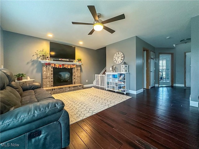 living room featuring dark wood-type flooring, ceiling fan, and a brick fireplace