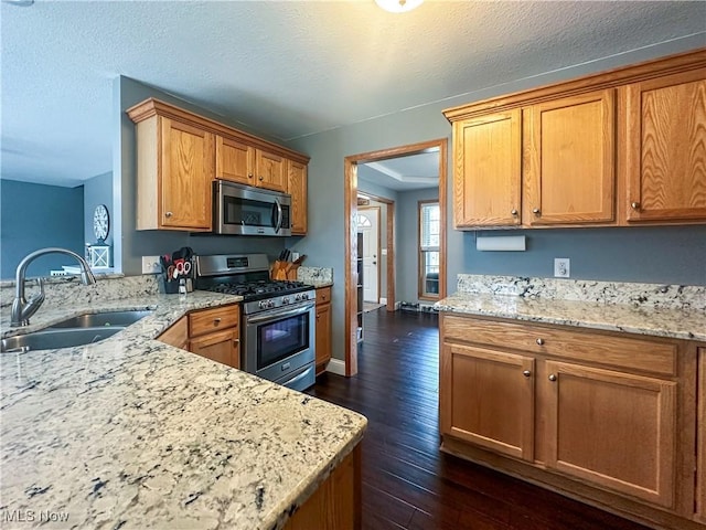 kitchen featuring a peninsula, appliances with stainless steel finishes, brown cabinetry, and a sink