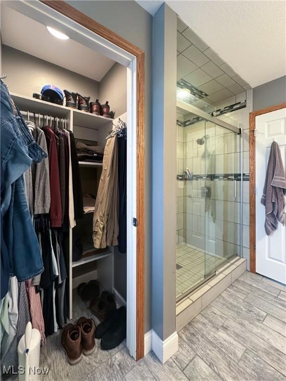 interior space with a stall shower, a spacious closet, baseboards, and wood finished floors