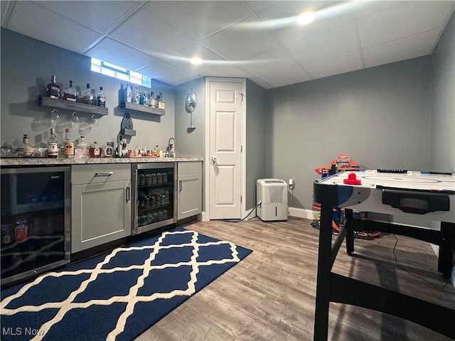 bar with wine cooler, a paneled ceiling, and light hardwood / wood-style flooring