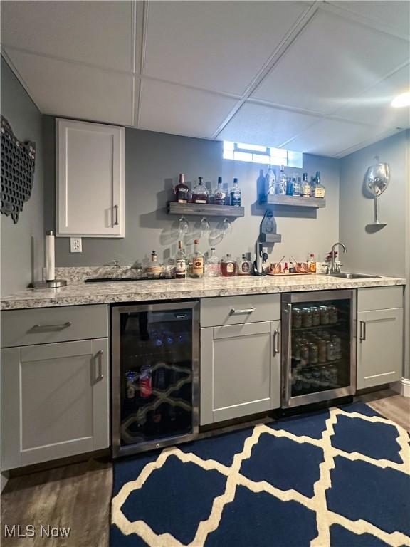 bar with dark wood-style floors, beverage cooler, wet bar, and a drop ceiling