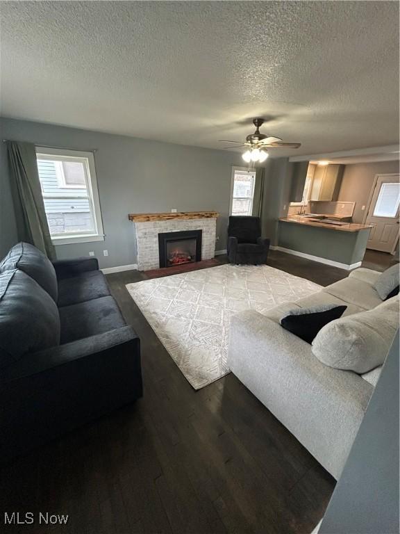 living room with ceiling fan, a brick fireplace, a textured ceiling, and dark hardwood / wood-style flooring