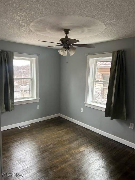 unfurnished room featuring a textured ceiling, dark wood-type flooring, and a healthy amount of sunlight