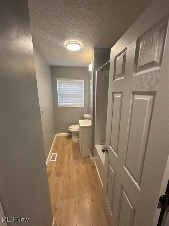 bathroom featuring toilet, a shower, wood-type flooring, a textured ceiling, and vanity