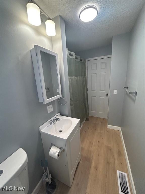 bathroom featuring hardwood / wood-style floors, vanity, a textured ceiling, curtained shower, and toilet