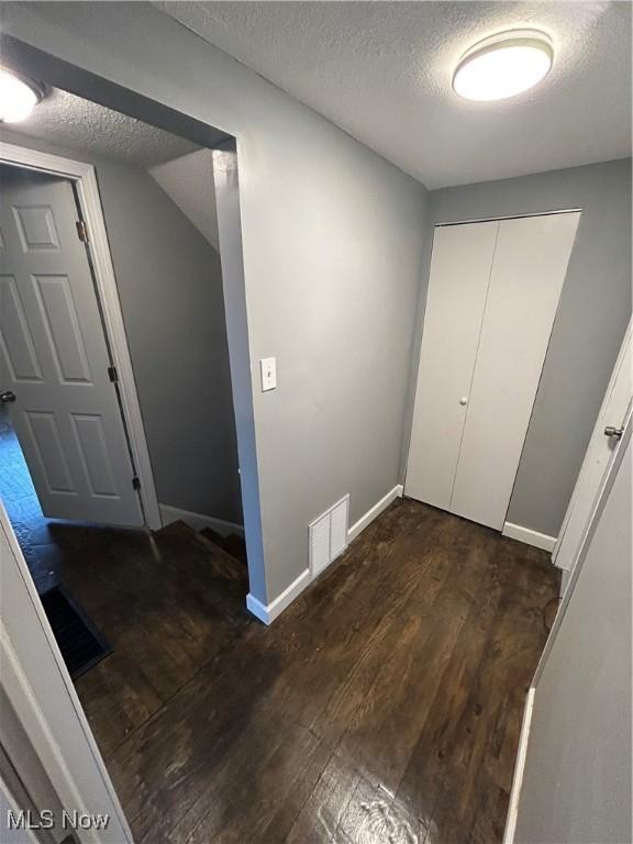 hallway with dark hardwood / wood-style floors, vaulted ceiling, and a textured ceiling