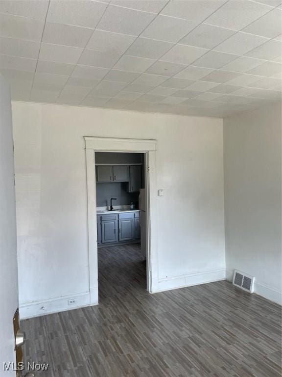 unfurnished room featuring a paneled ceiling, sink, and dark wood-type flooring