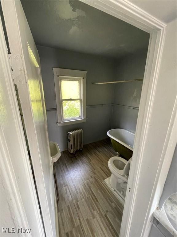 bathroom with radiator, hardwood / wood-style flooring, a bath, and toilet