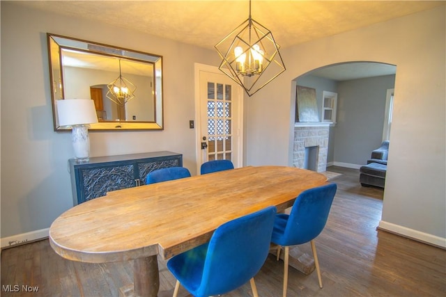 dining space featuring a stone fireplace, dark hardwood / wood-style floors, and a notable chandelier