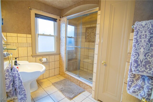 bathroom with tile walls, a shower with shower door, and tile patterned floors