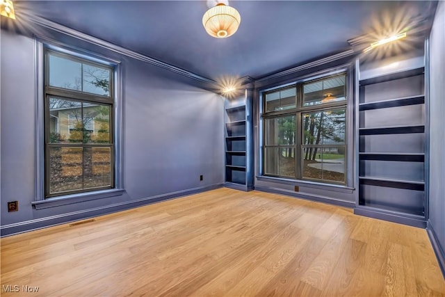 empty room with crown molding, light hardwood / wood-style flooring, and built in shelves