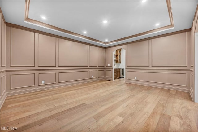 spare room with crown molding, light wood-type flooring, and a tray ceiling