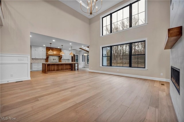 unfurnished living room featuring an inviting chandelier, a fireplace, light hardwood / wood-style flooring, and a high ceiling