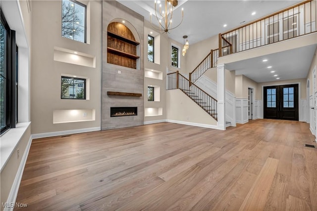 unfurnished living room with french doors, a notable chandelier, light hardwood / wood-style flooring, and a high ceiling