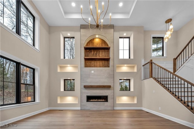 unfurnished living room featuring hardwood / wood-style floors, a fireplace, a high ceiling, a tray ceiling, and an inviting chandelier