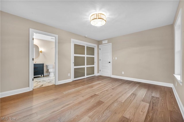 unfurnished bedroom featuring ensuite bathroom and light hardwood / wood-style floors