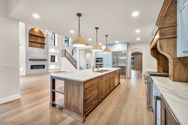 kitchen with sink, a spacious island, high quality appliances, light stone countertops, and decorative light fixtures