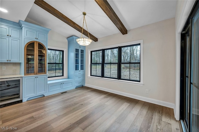 unfurnished dining area featuring a healthy amount of sunlight, beverage cooler, light hardwood / wood-style floors, and vaulted ceiling with beams