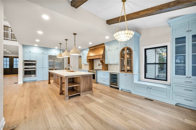 kitchen featuring wine cooler, premium range hood, high end appliances, hanging light fixtures, and a center island with sink