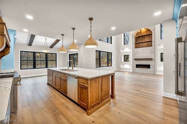 kitchen featuring pendant lighting, an island with sink, sink, stainless steel dishwasher, and light stone countertops