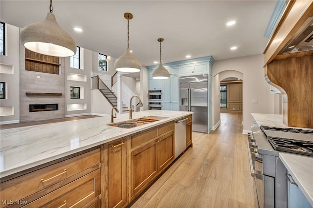 kitchen with pendant lighting, sink, high end appliances, light stone counters, and light hardwood / wood-style floors