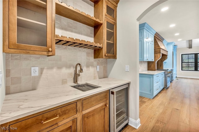 kitchen featuring sink, light stone counters, high end stainless steel range oven, beverage cooler, and light hardwood / wood-style floors