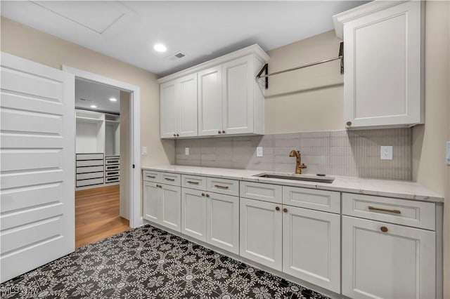 kitchen featuring sink, light hardwood / wood-style flooring, backsplash, light stone countertops, and white cabinets