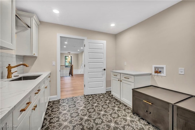 interior space featuring tasteful backsplash, sink, light stone countertops, and white cabinets